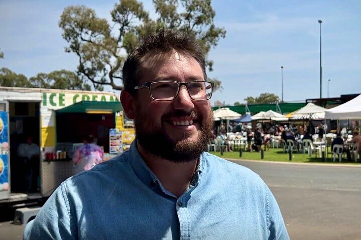 Man in glasses smiles in front of ice cream van and festival tables