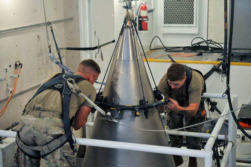 Two airmen work to secutre the titanium shroud at the top of a Minuteman III intercontinental ballistic missile