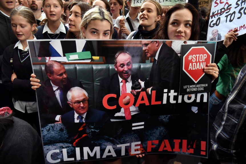 Two young girls in school uniforms hold up a sign criticising the Coalition at a climate protest