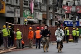 People ride bicycles past workers setting up barriers along the street.