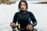 Woman in wetsuit, wait-deep in water, holding abalone.