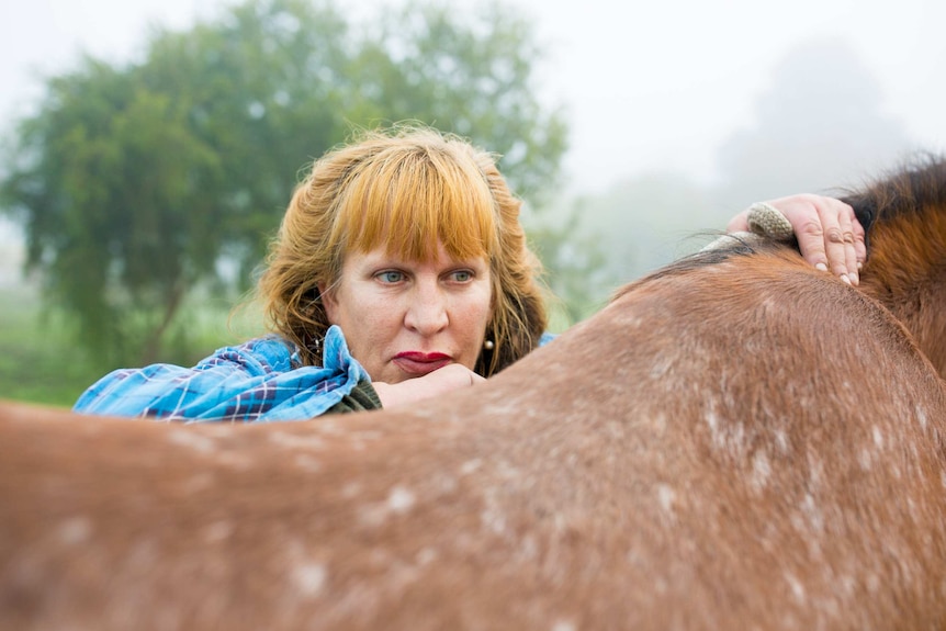 A woman's face can be seen behind the hind of a horse