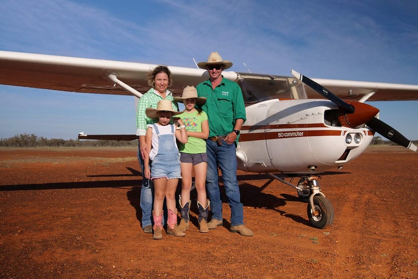 Young family stand in front of their light plane under a blue outback sky