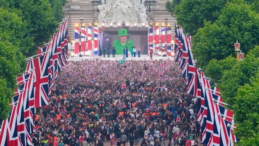 Crowds are seen on The Mall with Queen Elizabeth II shown on a screen.