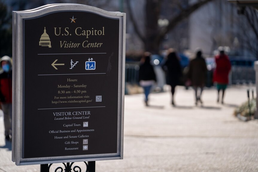 A sign that says US Capitol Visitor Center is in focus. A group of women walking are out of focus in the background