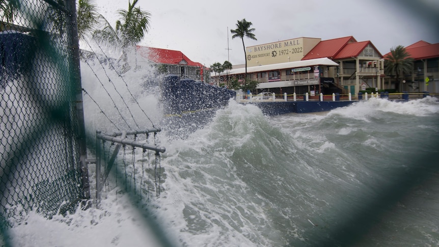 Waves crash against a dea wall and buildings. 