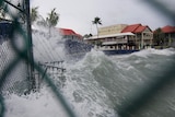 Waves crash against a dea wall and buildings. 