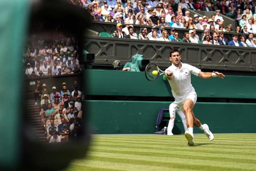 Novak Djokovic reaches to his right to get his racquet to the ball for a forehand return, as the crowd watches behind him.