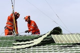 Two men wearing orange high-vis and helmets on a rooftop where tiles have been ripped off.