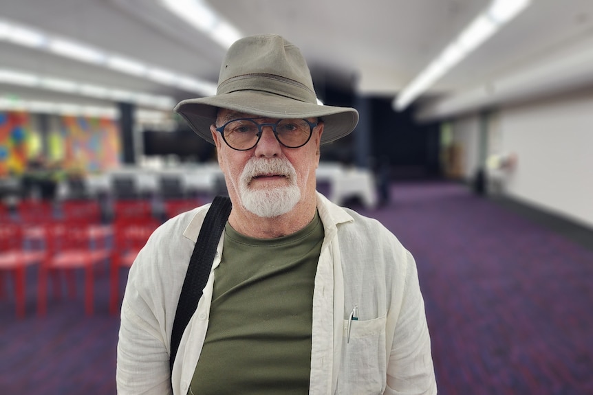 man wearing glasses and hat, bag slung over shoulder, indoors