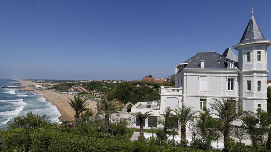 Une grande maison se trouve sur une colline pittoresque surplombant une plage de Biarritz.