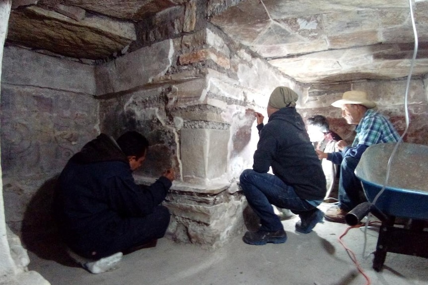 Three workers carefully brush dirt and debris from buried ancient structures.