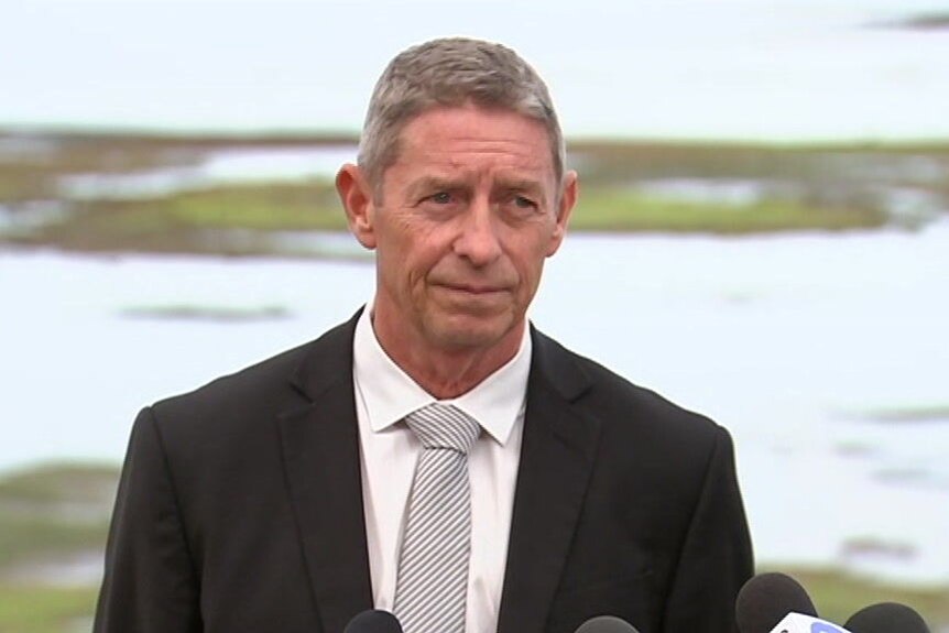 Maurie Ryan, dressed in a suit, addresses journalists at a media conference in front of the Ricketts Point foreshore.