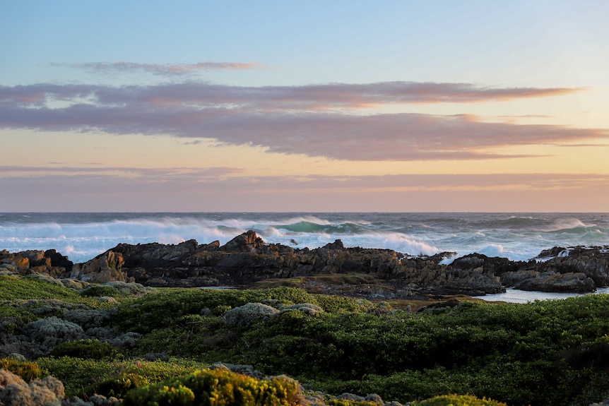 Ocean waves gently crash onto rocks at dusk