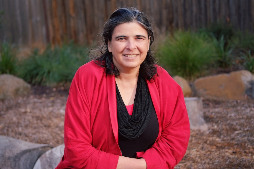 Researcher and writer Shakira Hussein wearing a black top and red cardigan, sitting in a yard.