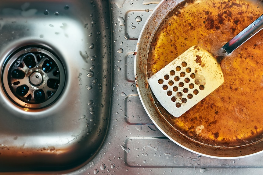 在厨房下水道旁看到一个煎锅，里面装满了脏兮兮的食用油和锅铲
