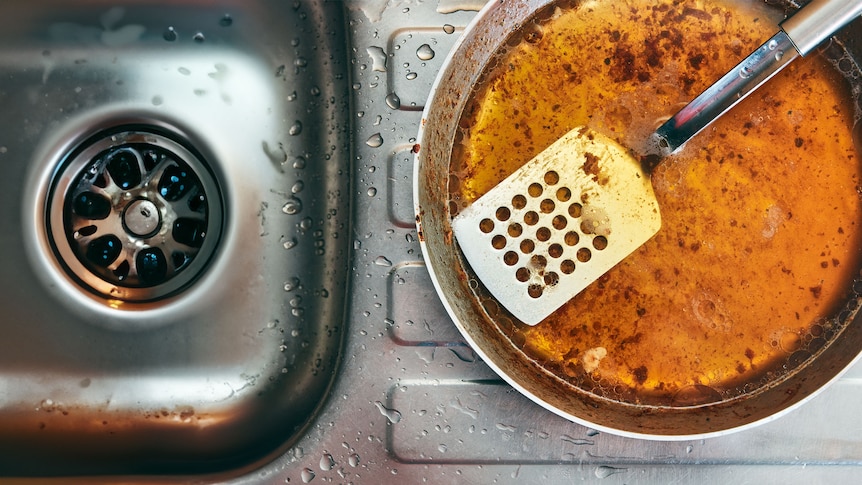 A view of a frying pan filled with dirty cooking oil and a spatula, next to a kitchen drain
