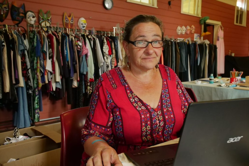 Veronica Abbott using a laptop, she is wearing a bright red top and looking at the camera.