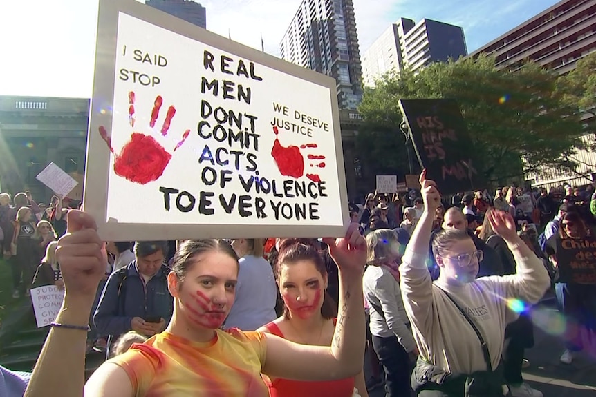 A woman holding a sign protesting violence against women