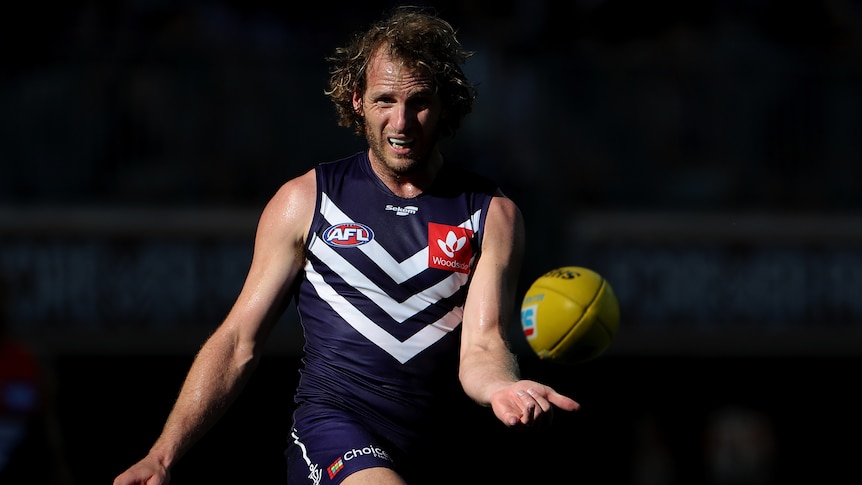 A Fremantle AFL kicks the ball with his right foot.