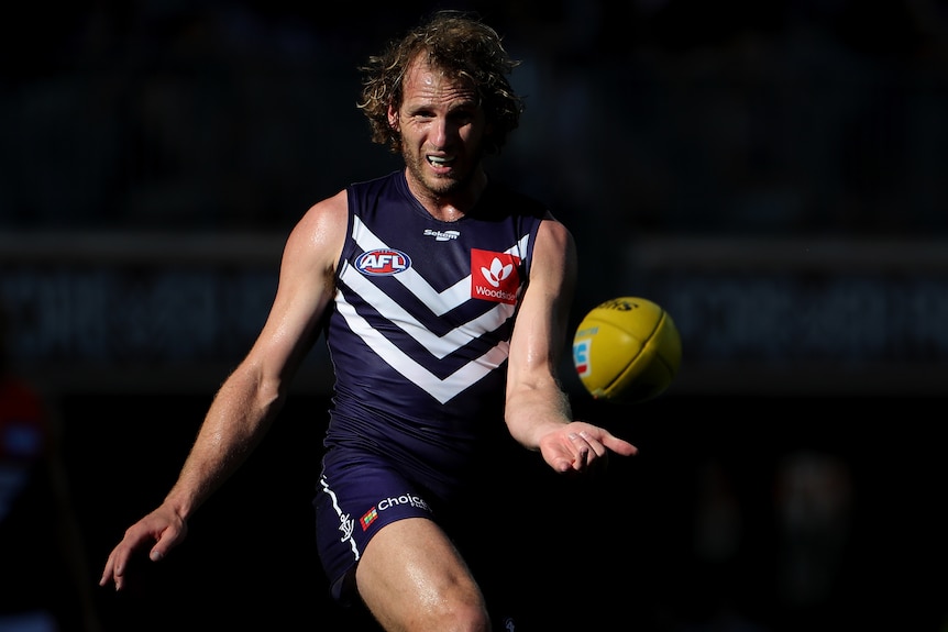 A Fremantle AFL kicks the ball with his right foot.