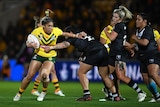 An Australian rugby league player grimaces as she tries to fend off the tackle of a New Zealand defender.