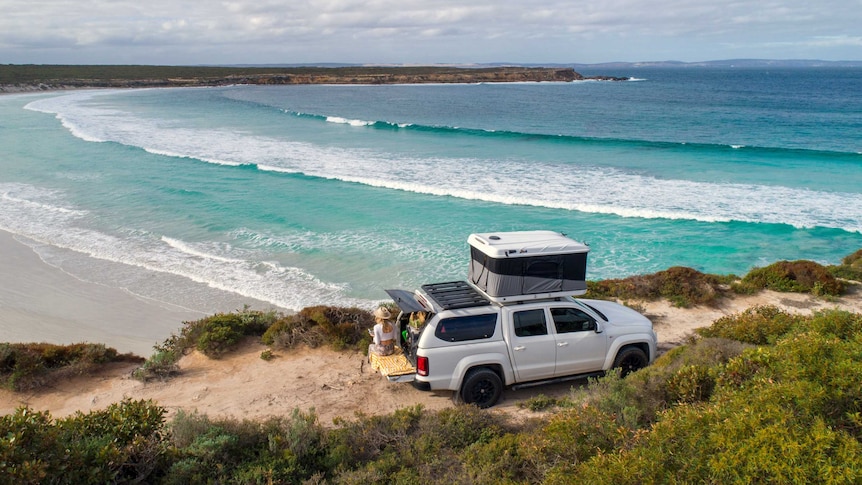 A white four-wheel-drive looks over crystal blue water and land mass in the distance.