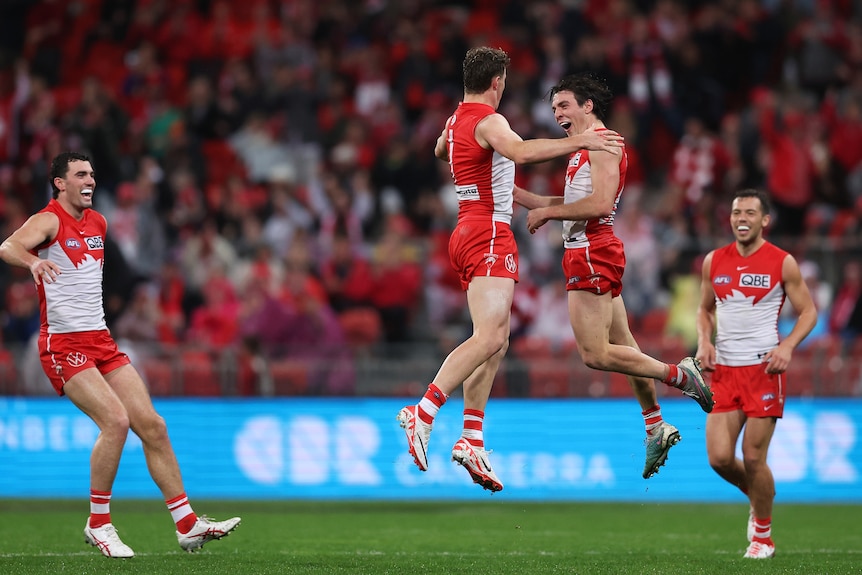 Two Sydney Swans AFL players leap high in the air to bump into each other in celebration after a goal.