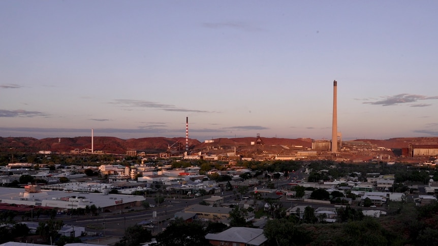 The rooves of buildings and three smelter stacks from the Mount Isa mine against a blueish purple sky 