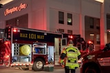 A person wearing a hazmat jacket stands in front of a hazmat truck parked outside a hotel at night.