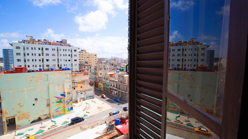 View of a vibrant streetscape in Havana from a hotel window. Vintage cars and colonial buildings can be seen in the background.