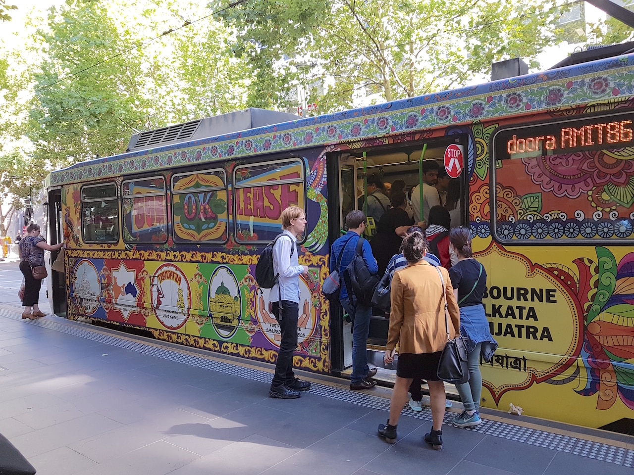 Un tranvía decorado con un arcoíris en una parada en Melbourne con gente subiendo