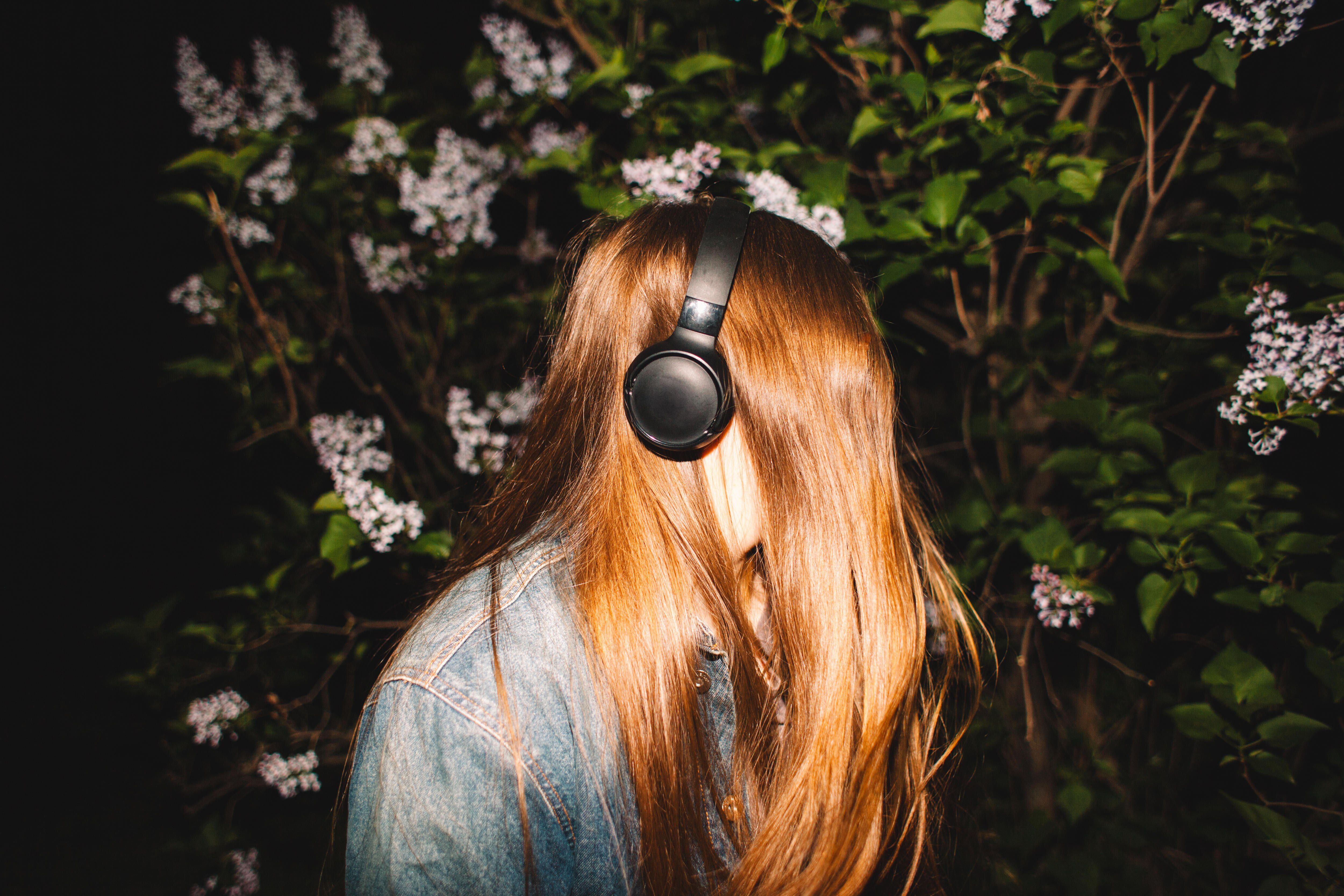 Image of a young woman wearing over-ear headphones. Her hair is covering her face.
