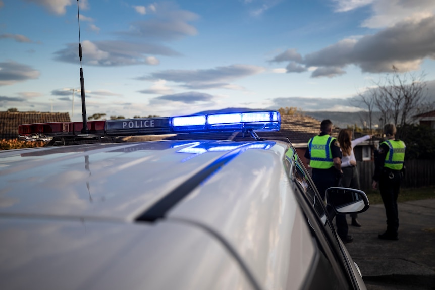 Three people standing in front of a police car