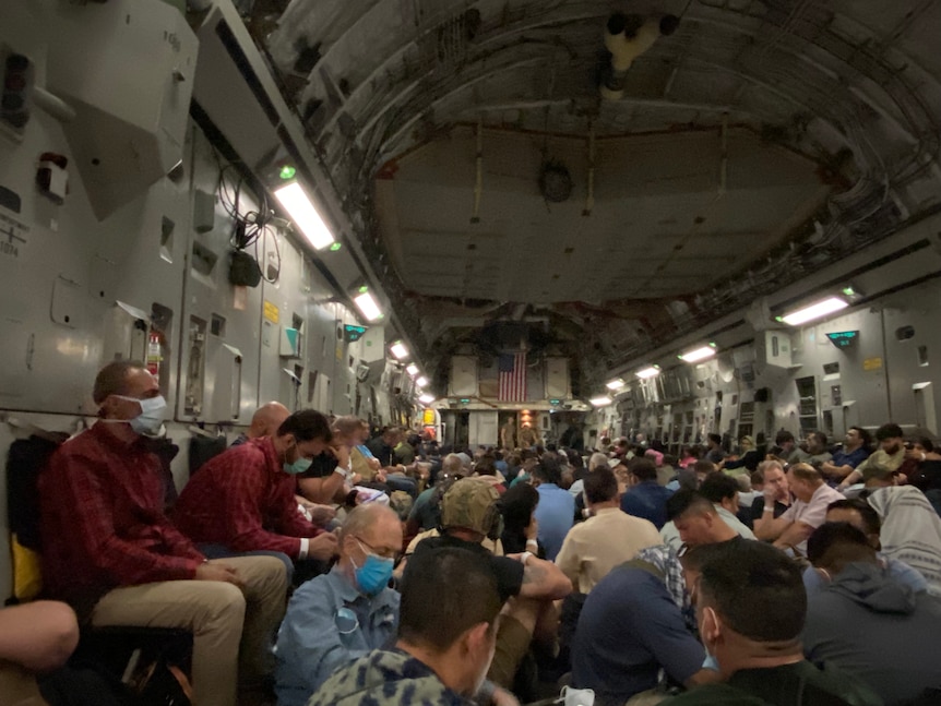 Hundreds of people sitting in the cargo hold of a C-17 plane.