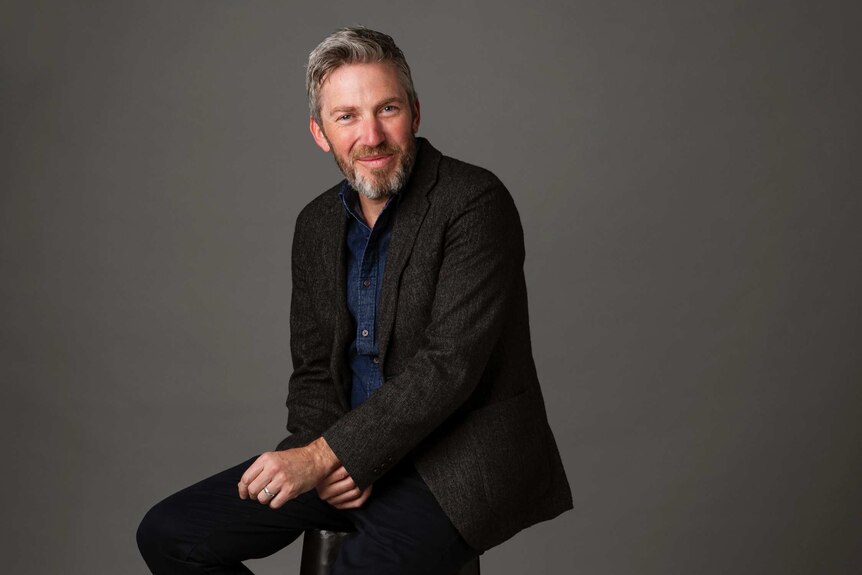 A man sits on a stool and smiles for the camera