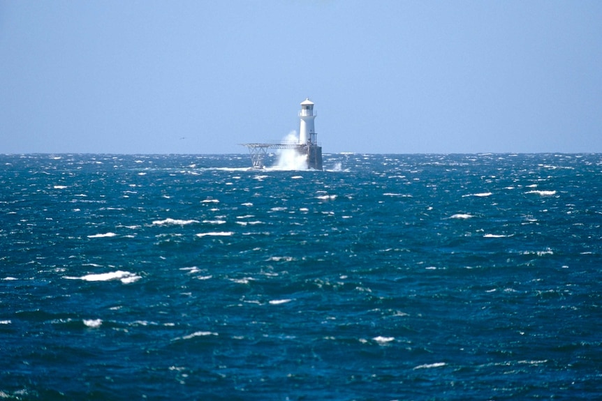 A lighthouse surrounded by whitecapped ocean.