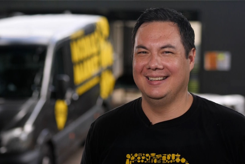 A man in a black shirt with a black truck with yellow writing in the background