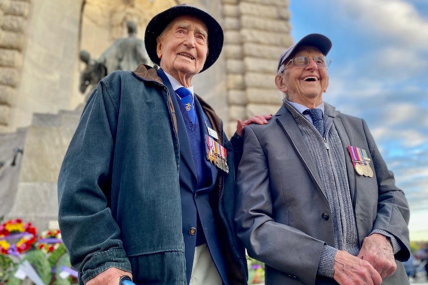 Two veterans stand in front of a war memorial.