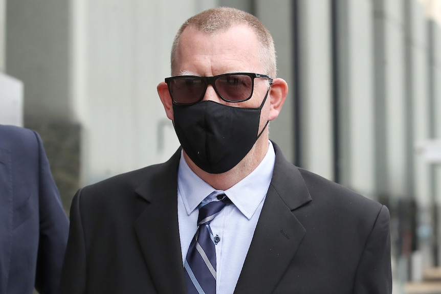 A man with dark black sunglasses and black mask.