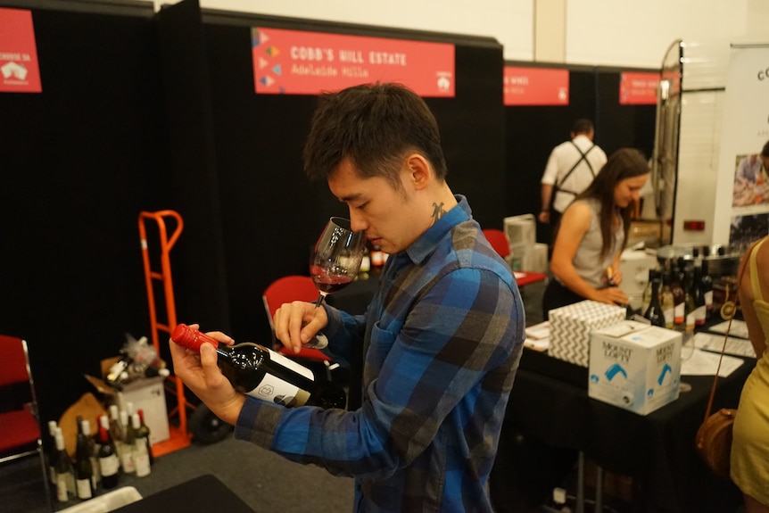 A man looks down at a wine bottle at an expo.