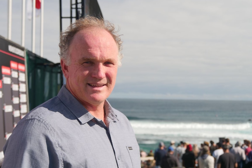 Andrew Stark se tient près de l'infrastructure de compétition de surf avec l'océan et les vagues en arrière-plan.