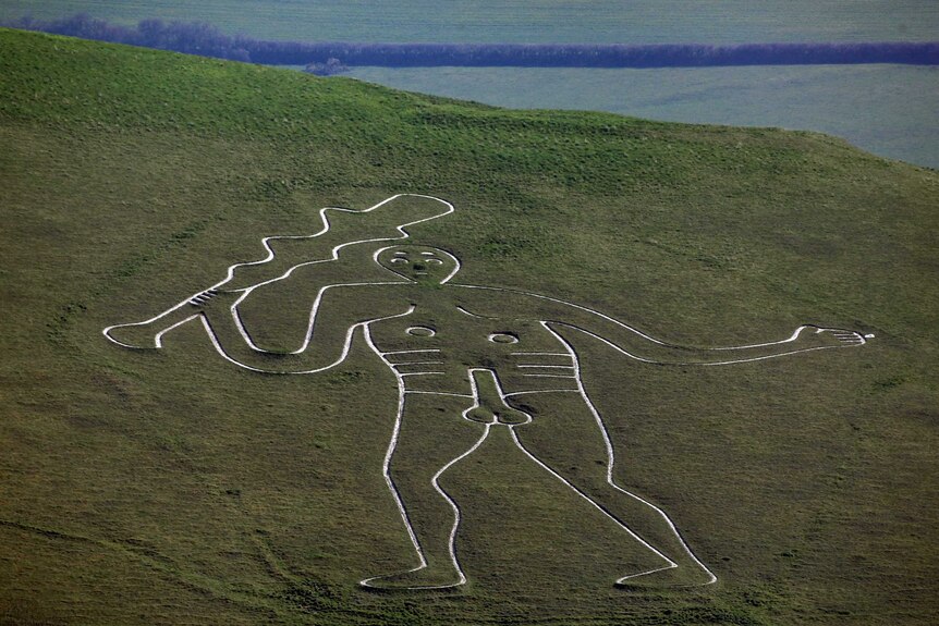 Telephoto landscape shot of a giant figure carved into a steep, green hillside.