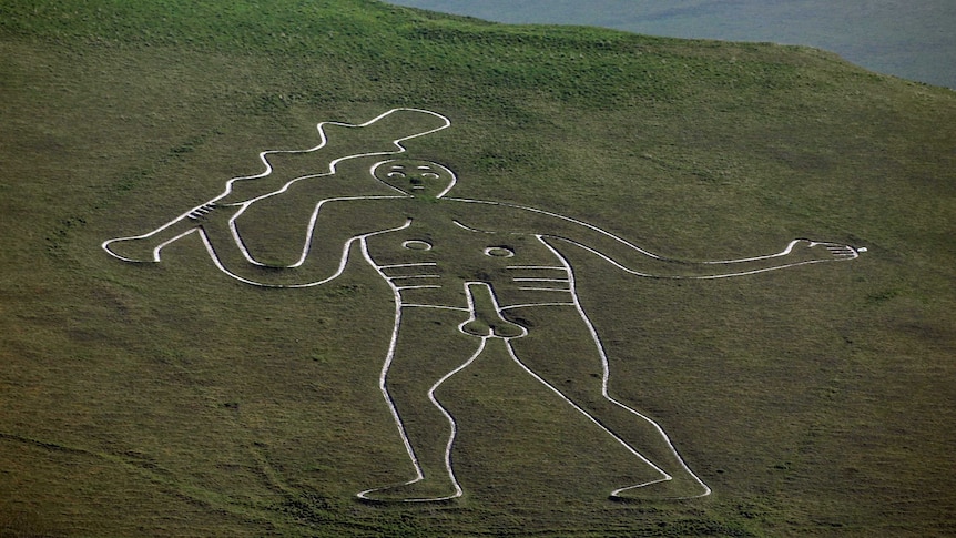 Telephoto landscape shot of a giant figure carved into a steep, green hillside.