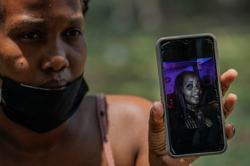A women holds her phone to the camera which displays a photo of her sister.