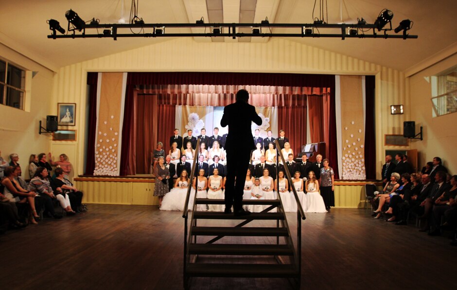 A photographer in silhouette stands on a stair to take a group photograph of the Mundulla debuntes and their partners.