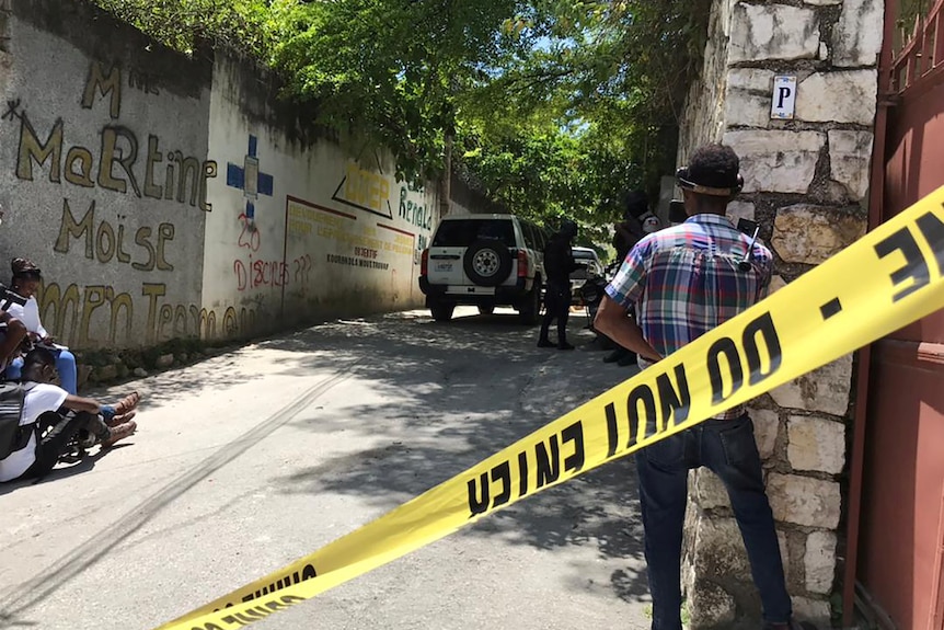 A man stands on a street with police tape.