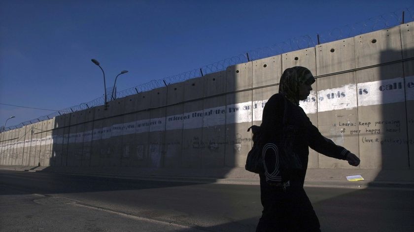 A Palestinian woman walks past the security barrier in al-Ram in the West Bank (Reuters: Baz Ratner)