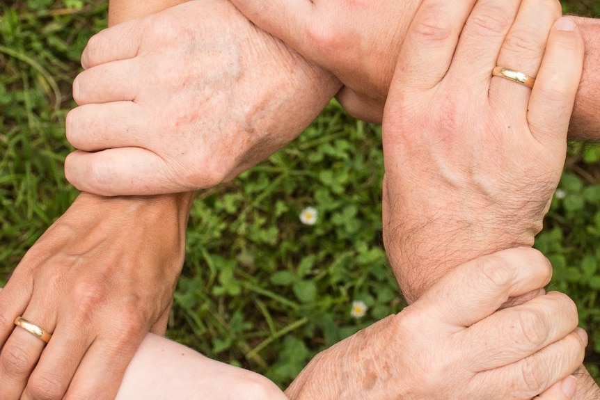 Six adult hands holding wrists of six arms to form a circle  