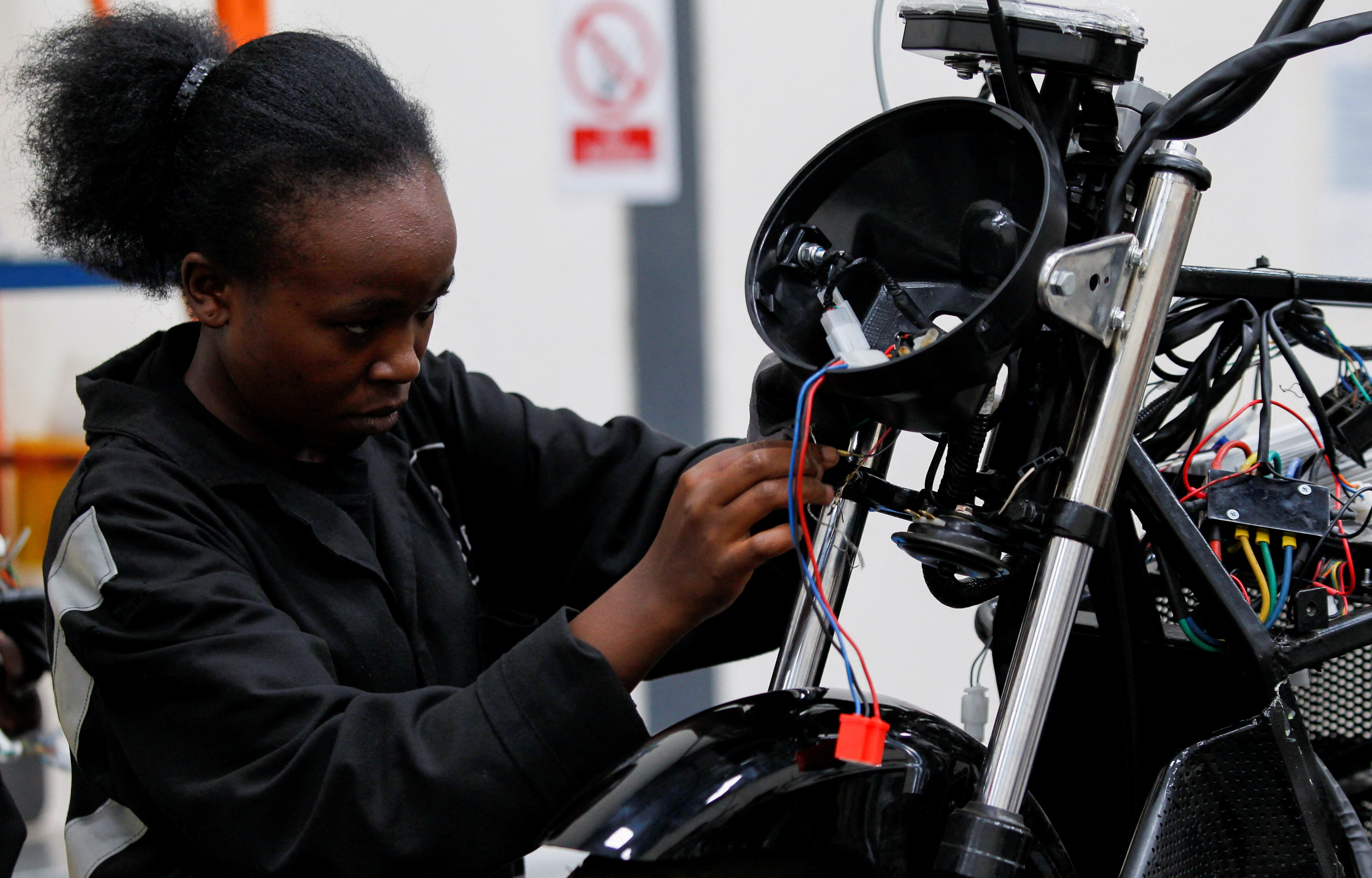 A woman works on a partially assembled motorcycle in a industrial setting